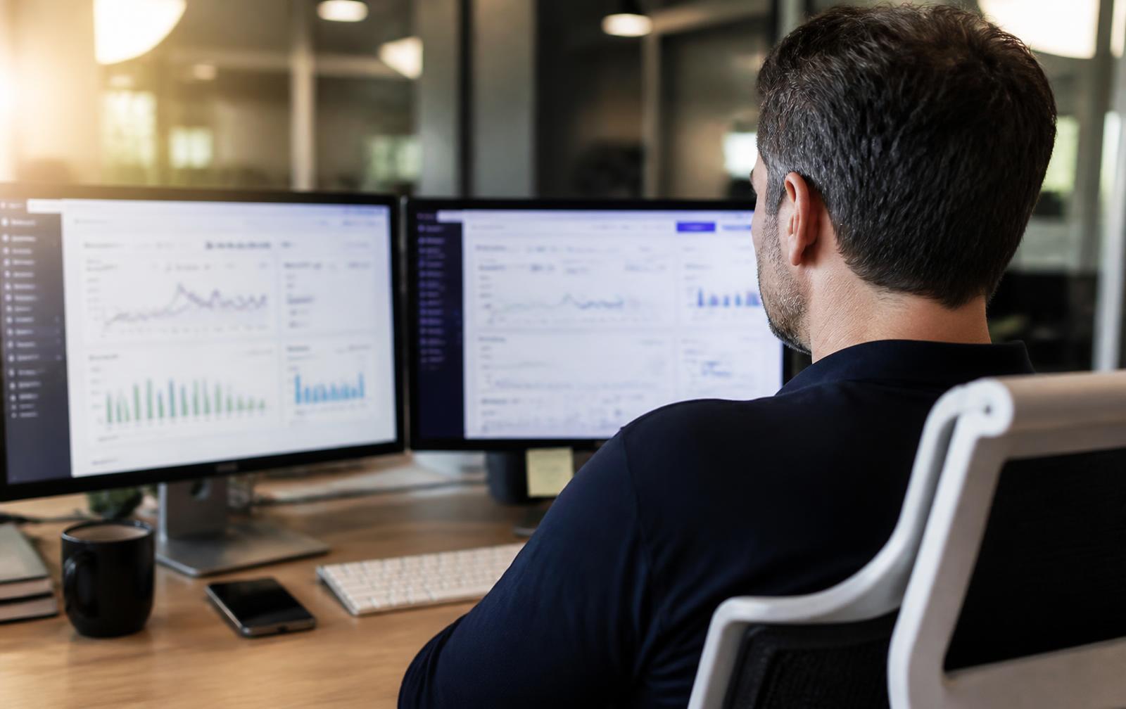 Marketer reviewing an ecommerce paid media dashboard on two monitors